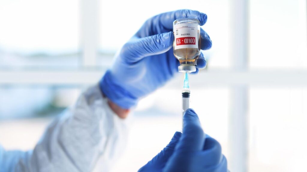 Nurse hands drawing COVID-19 vaccine out of vial into a needle to prep for booster shot.