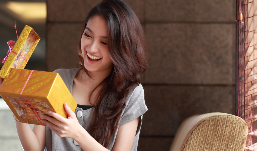 Young female travel nurse opening yellow present box and smiling excited at the gift.