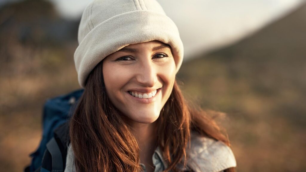 Brunette woman smiling outdoors while hiking in Michigan.