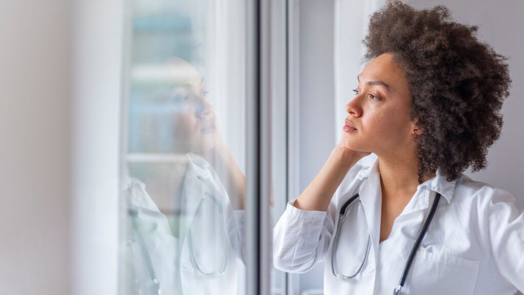 Sad female nurse in uniform staring out the window thinking.