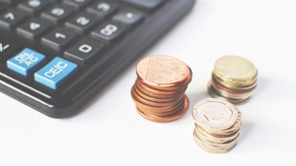 Calculator next to stack of coins on white background.
