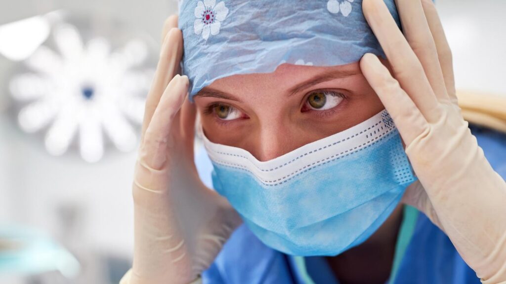 Frustrated female nurse with mask on and hands on her head experiencing burnout.
