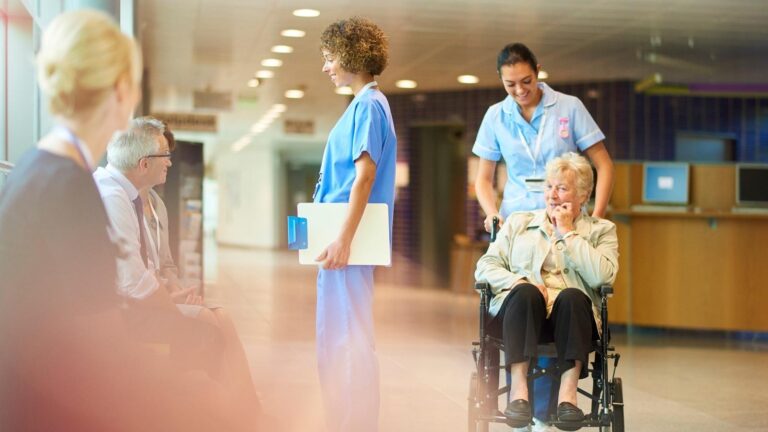 Post-acute care nurse pushing a senior in a wheelchair down a hall.