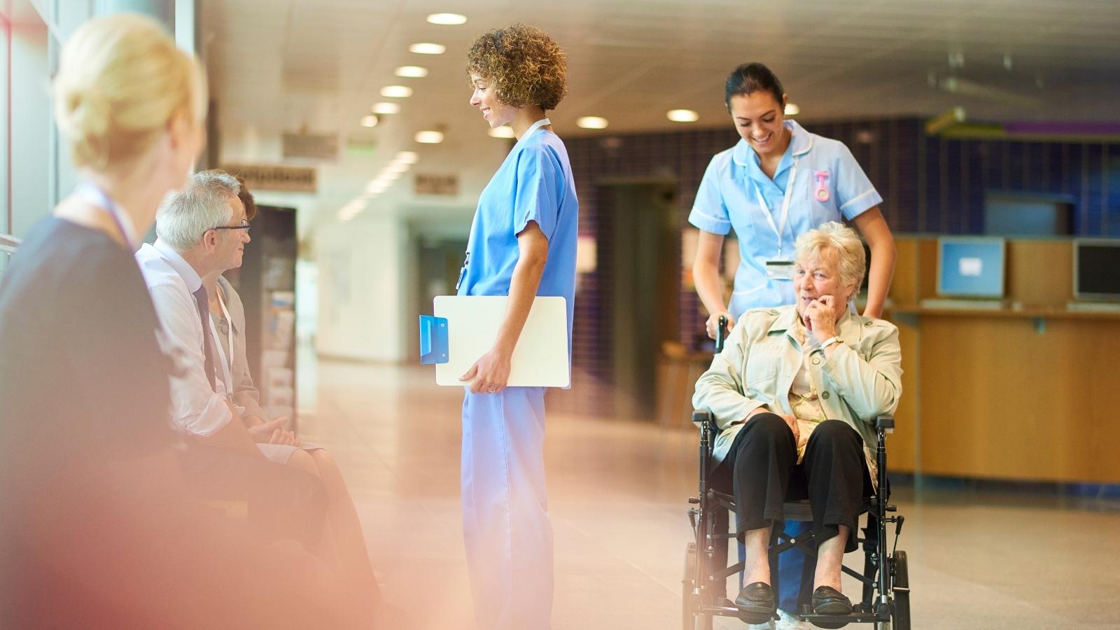 Post-acute care nurse pushing a senior in a wheelchair down a hall.