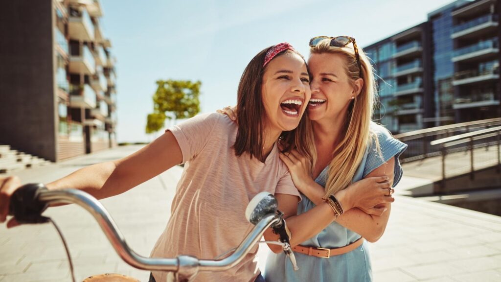 Two women outdoors smiling and riding a bike together while sharing funny nurse quotes.