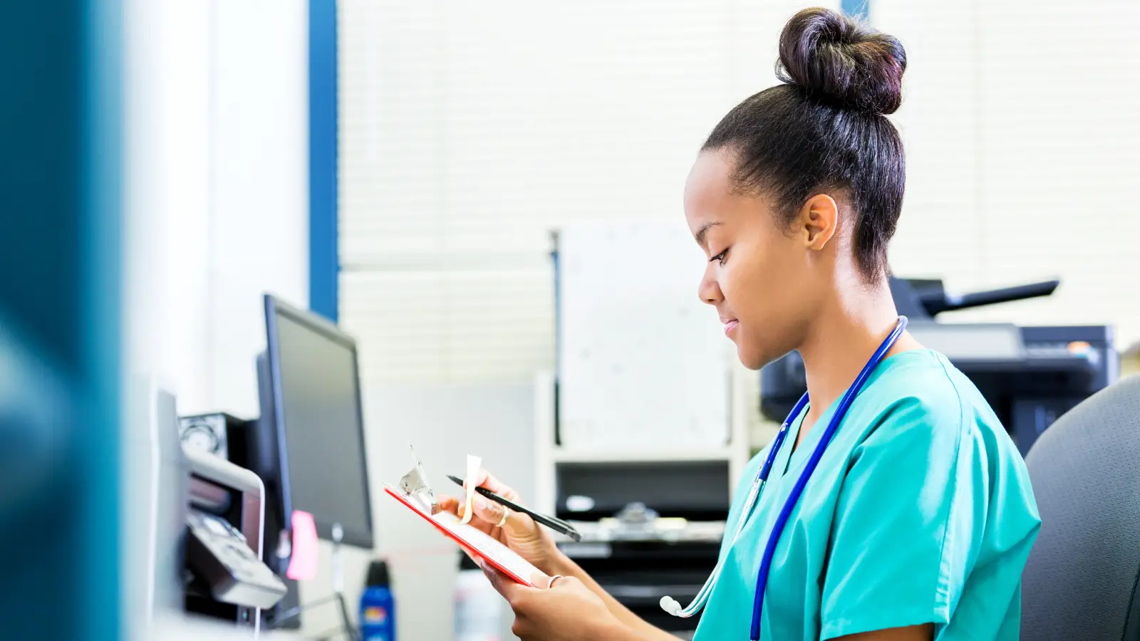 Travel nurse looking at a clipboard and sitting in an office at a table in post-acute-care