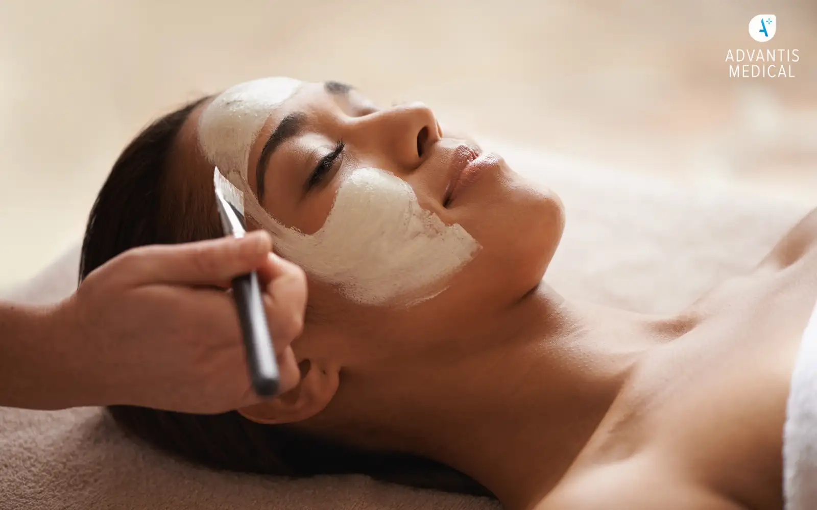 Female travel nurse woman lying down at a spa gift and getting a facial face mask painted on.