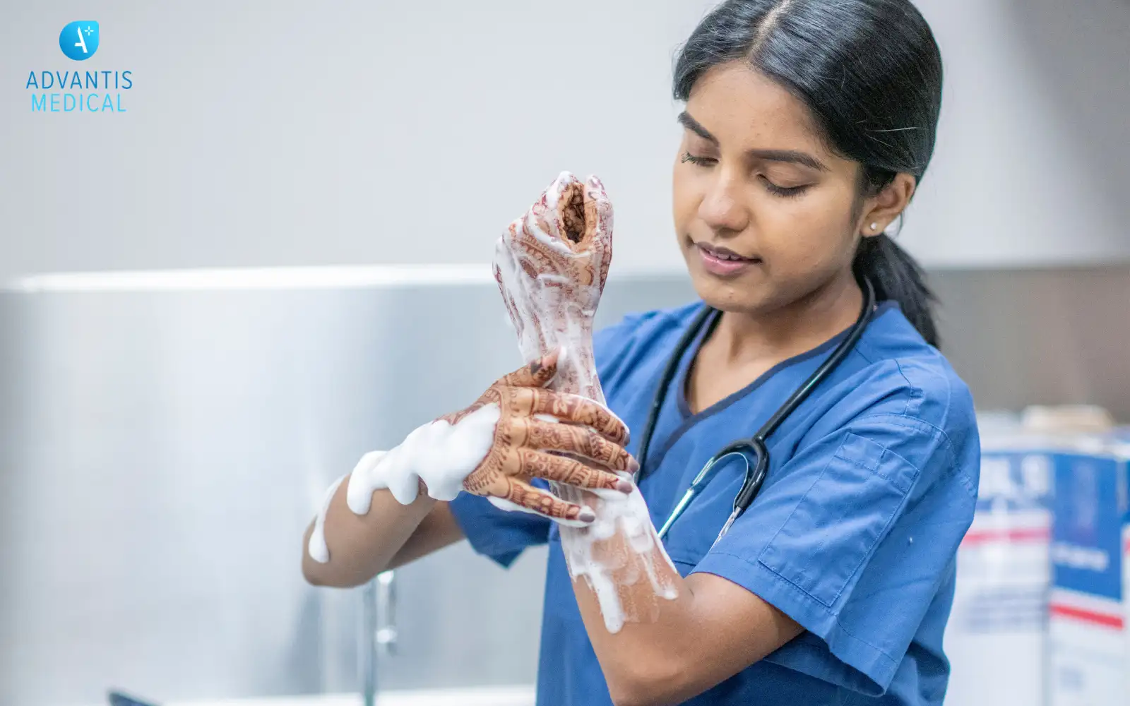 Female travel nurse in blue medical scrubs washing her ands and arms with soap.