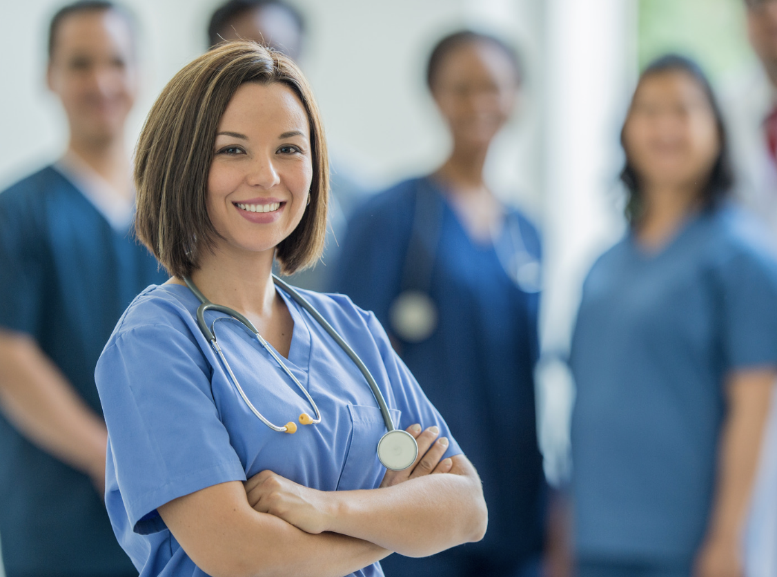 nurse smiles into camera. Other nurses being. Travel nursing in california