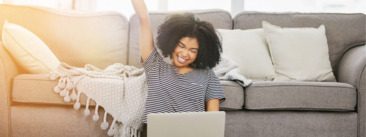 Traveler celebrating on a couch after booking housing on a laptop